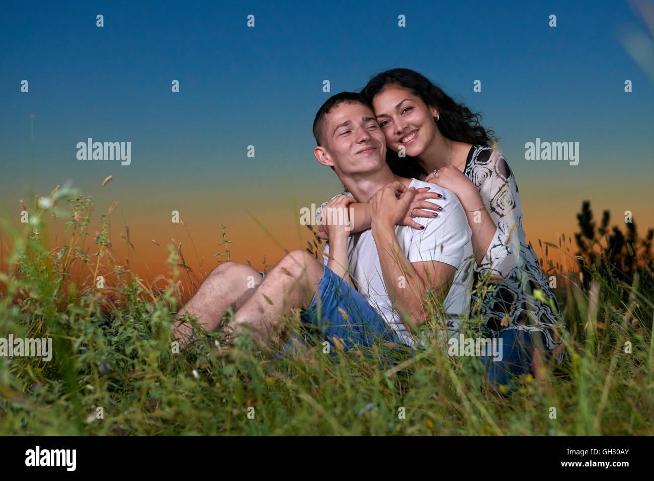 romantic couple sit on grass at sunset on outdoor, beautiful landscape ...