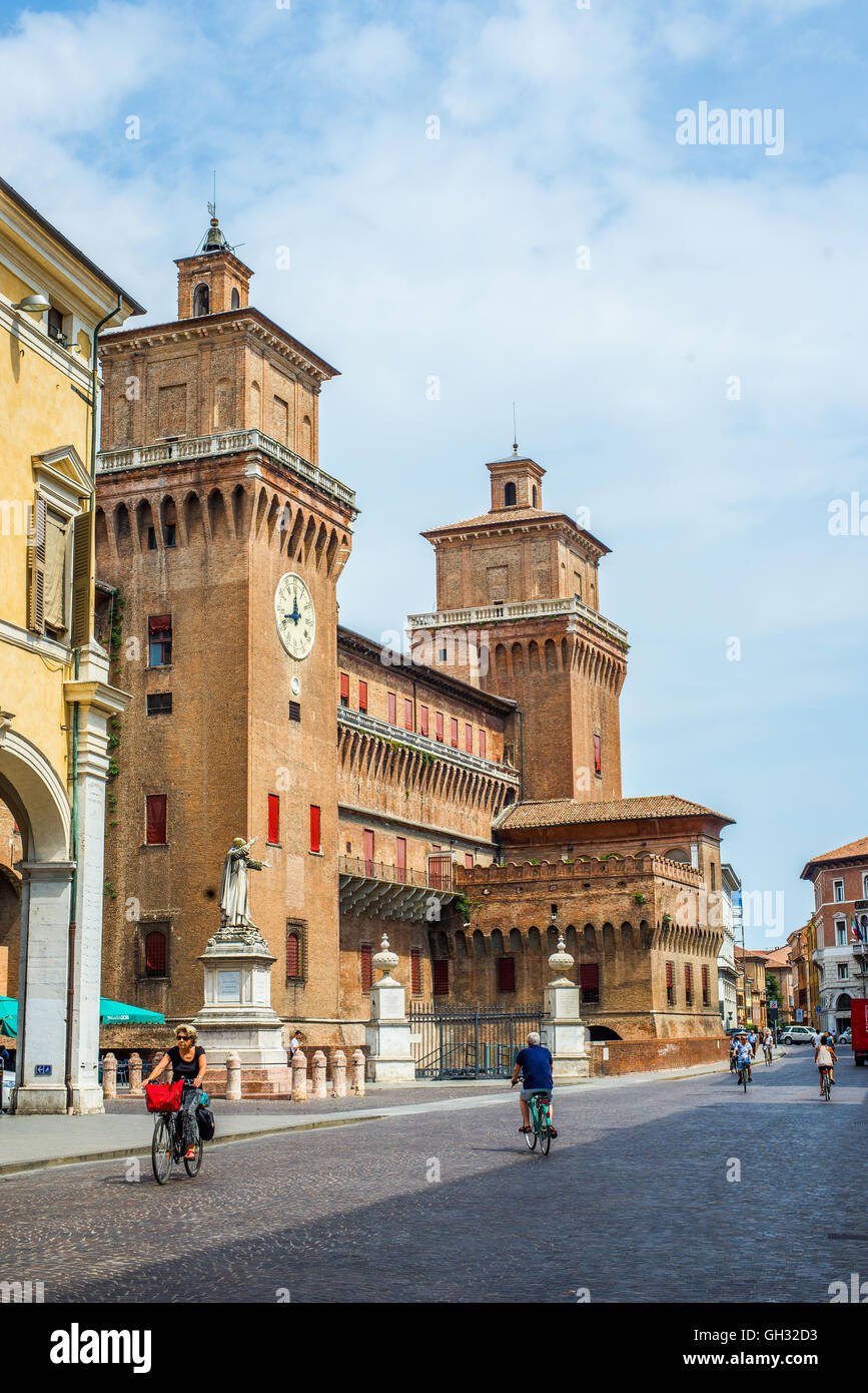 Cyclists crossing Corso Martiri della Liberta street with Estense castle in background. Ferrara, Italy. Stock Photo