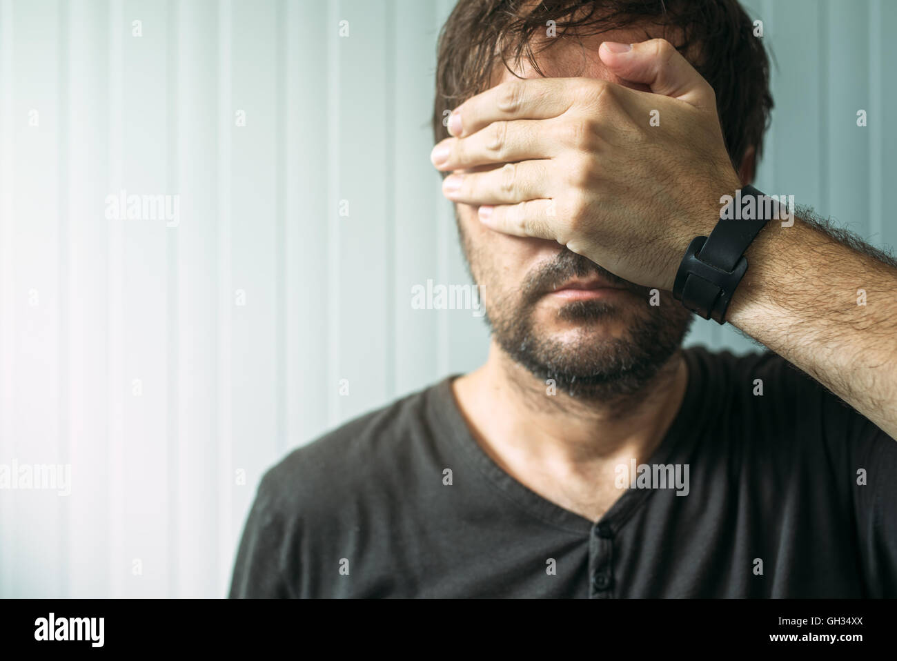 Portrait of casual adult male covering face and eyes with hand, selective focus Stock Photo