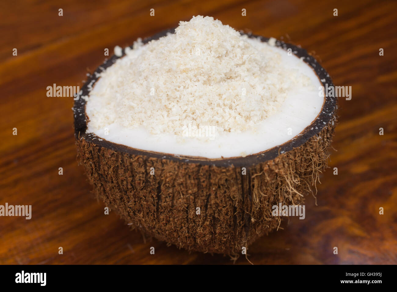 A coconut half with shredded coconut spilling out onto a wooden table