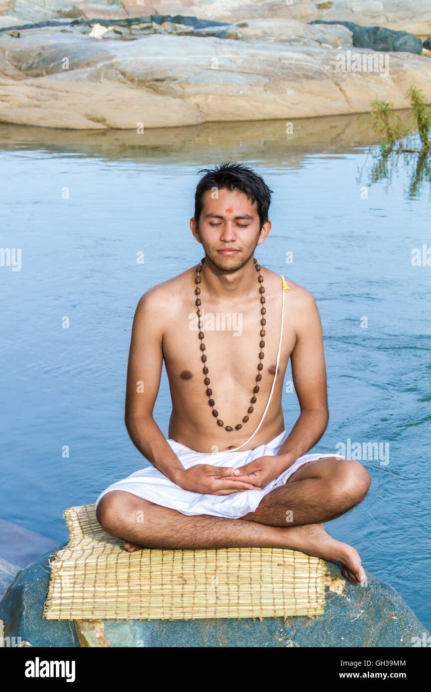 A young Hindu priest (brahmin), sits in meditation on a river bank. Stock Photo