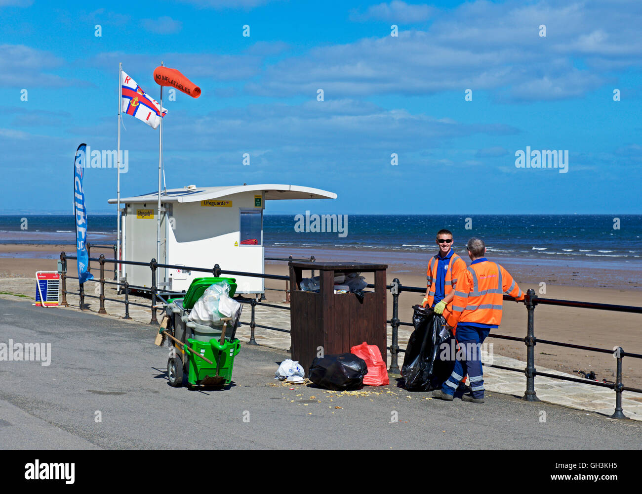 Two council workman and overflowing rubbish bin on the promenade at