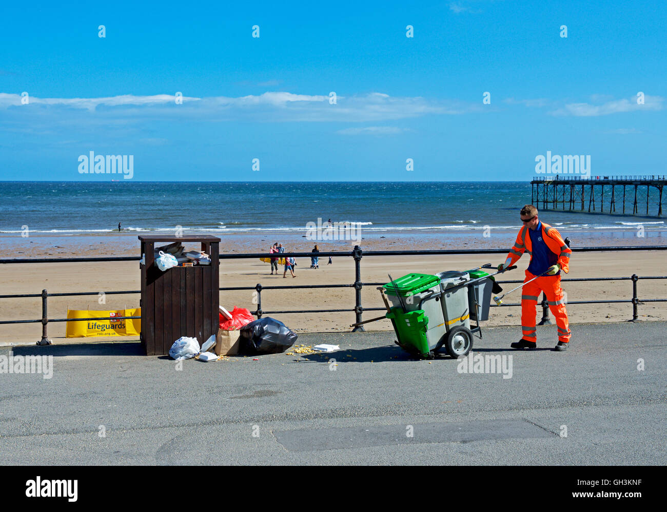 Council workman approaching overflowing rubbish bin on the promenade at