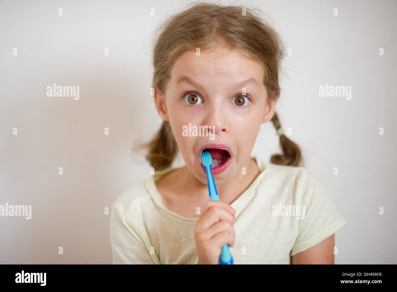 Cute girlie with pigtails diligently brushing his teeth. In a hand a