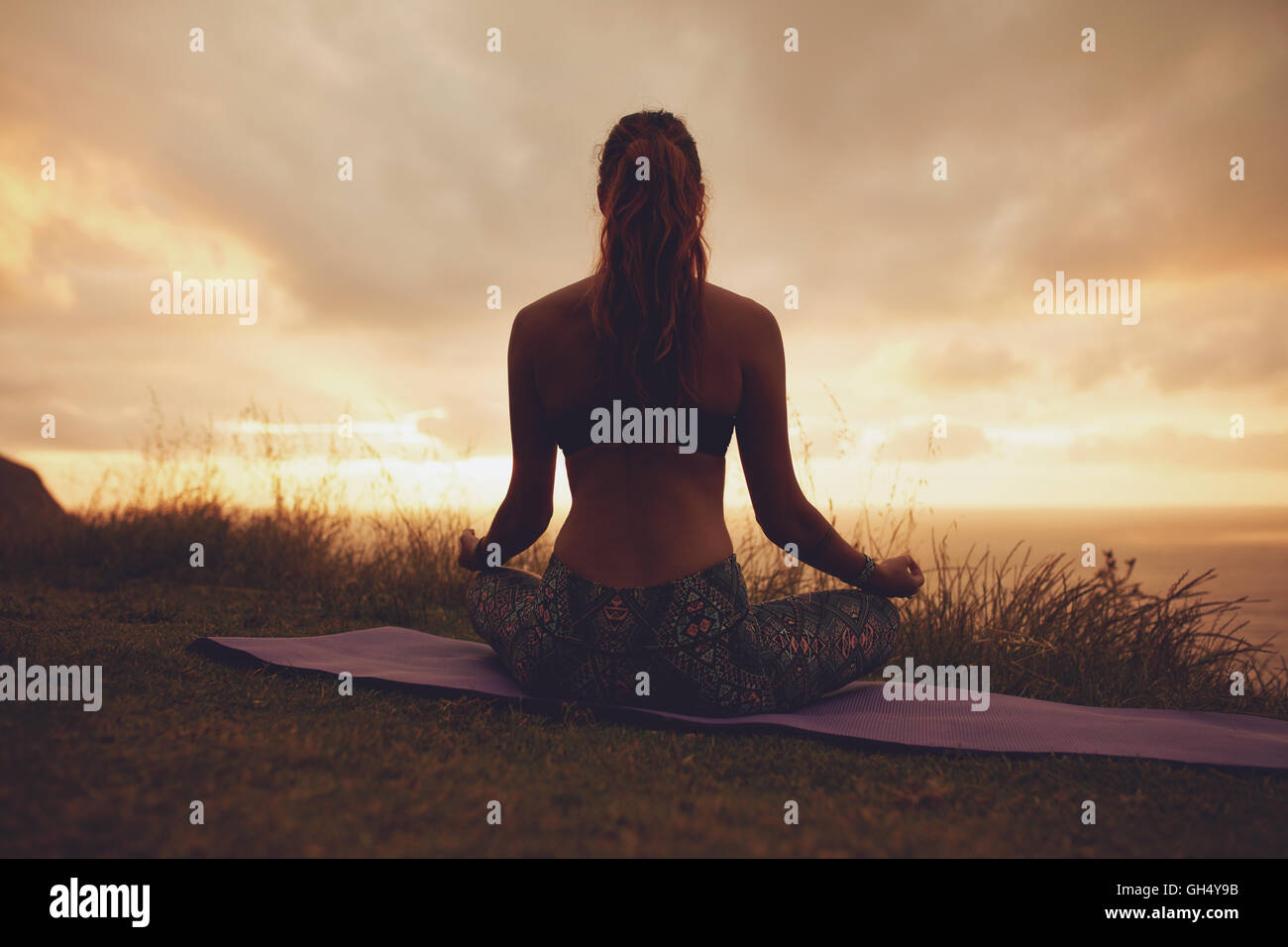 Silhouette rear view of young woman doing yoga meditation outdoors. fitness female model sitting on exercise mat in lotus yoga p Stock Photo