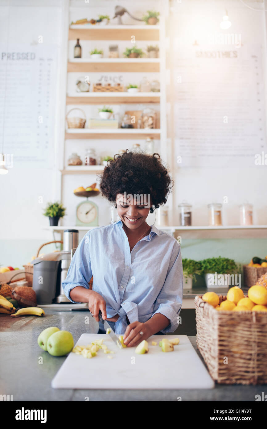 Vertical shot of african young woman cutting fruit on cutting board to make a fresh smoothie. African female bartender working a Stock Photo