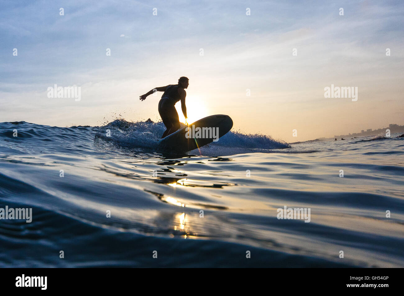 A surfer with a longboard riding a wave at sunset Stock Photo - Alamy