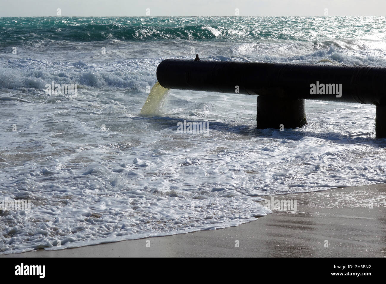Stormwater pipe flowing into the ocean across beach Stock Photo