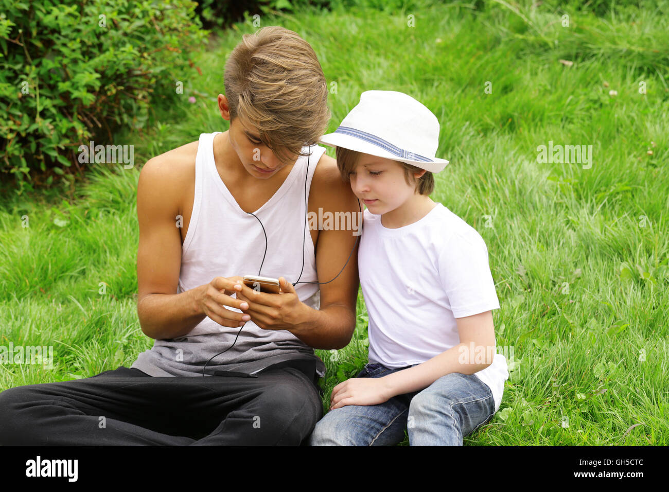 Senior and younger brother sitting on the grass and looking to the smartphone Stock Photo Alamy