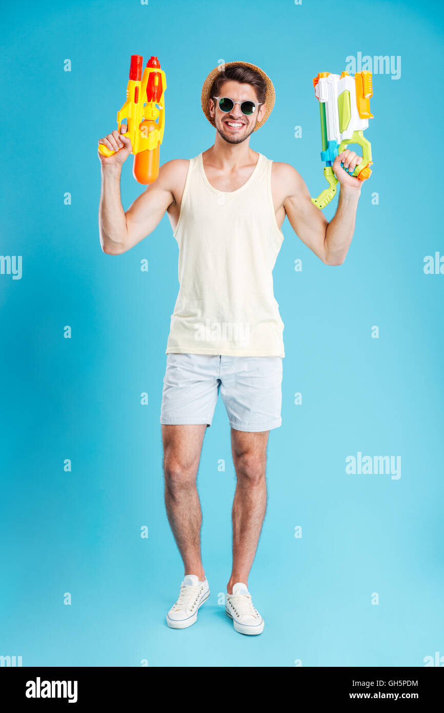 Full length of cheerful young man holding two water guns Stock Photo