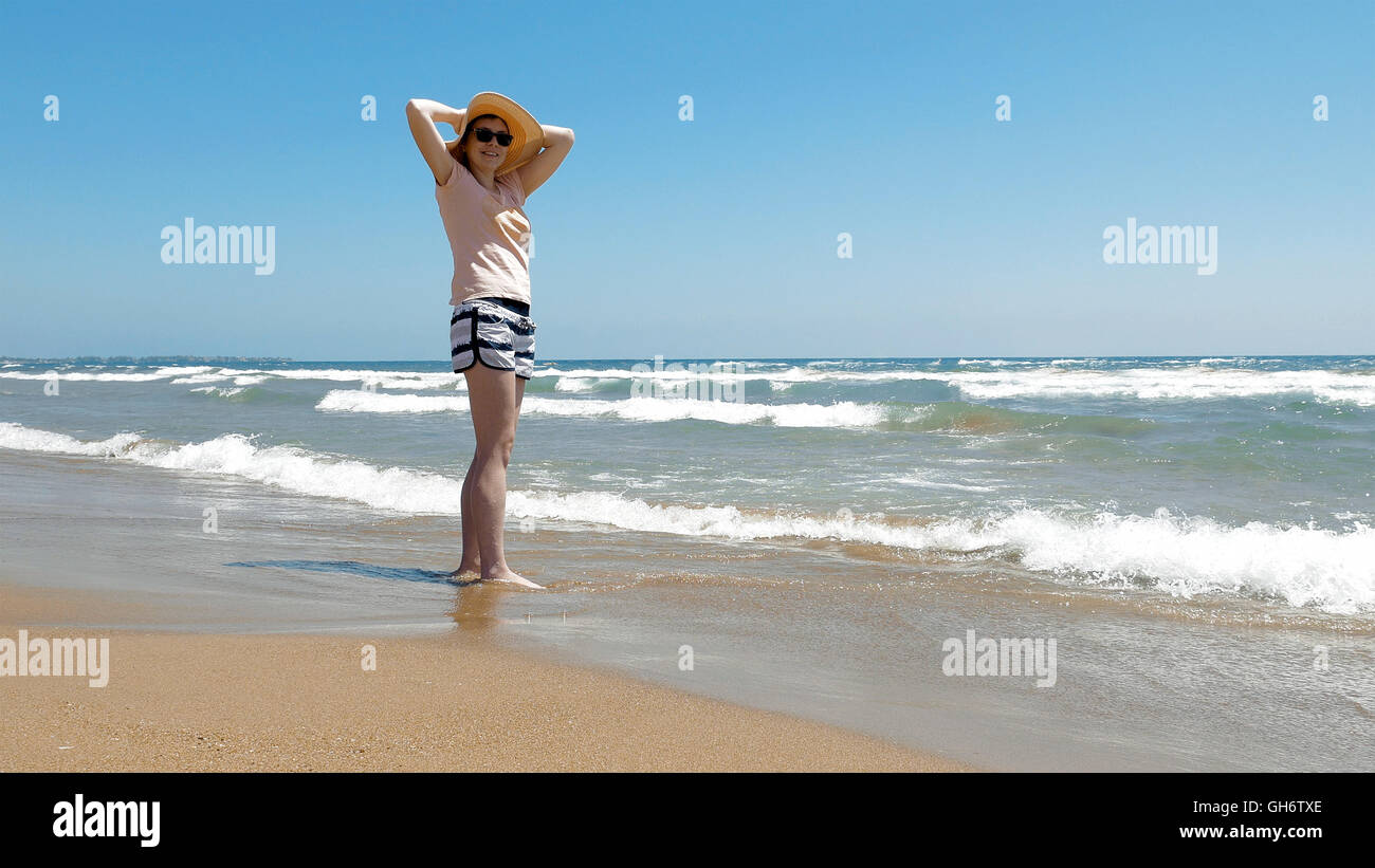 Woman is standing at the beach with jute hat on Stock Photo