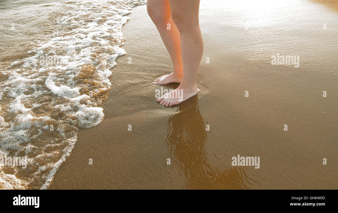 Female stands on wet sand and waves at the beach Stock Photo