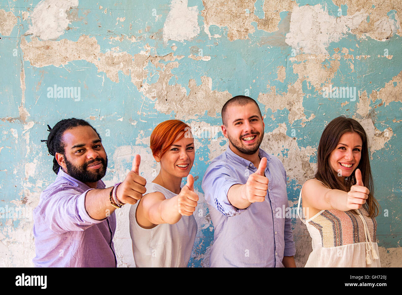 Young multiethnic people posing in front of a grunge wall with a thumbs up Stock Photo