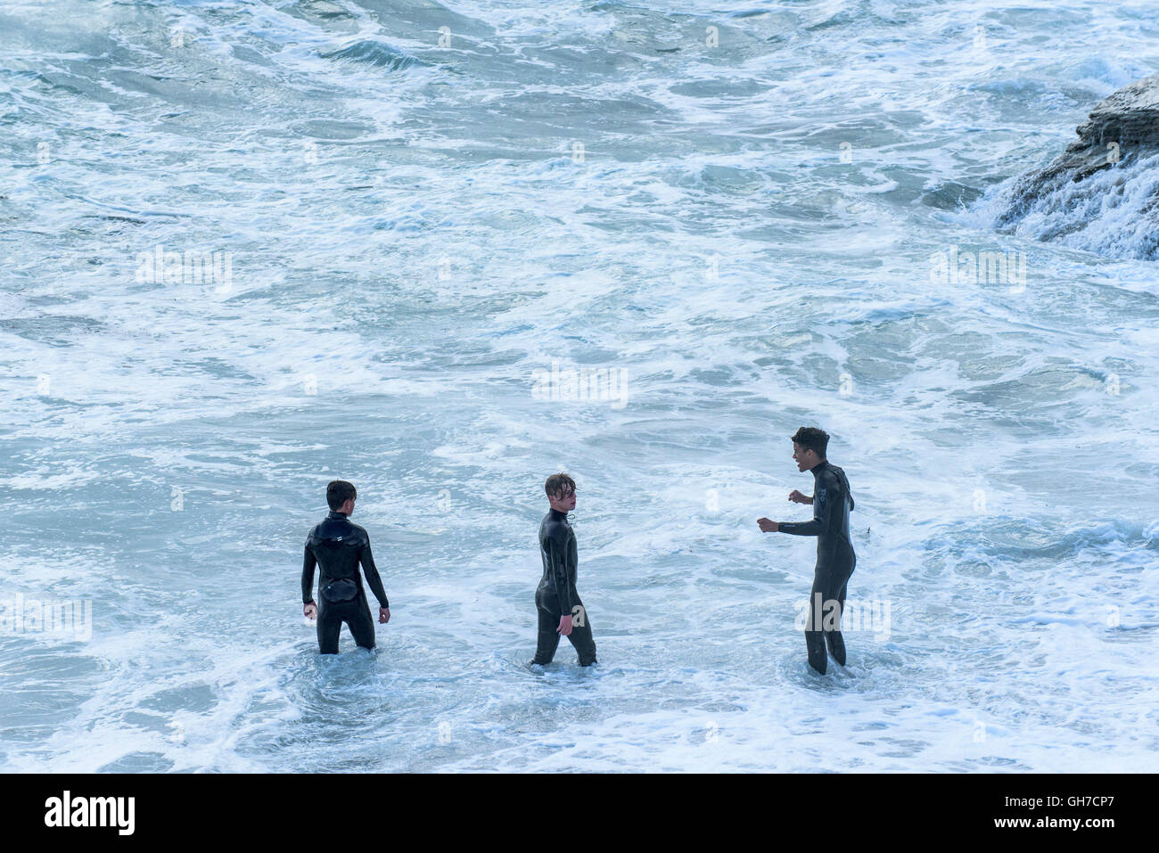 Three teenagers in wetsuits stand in the sea off the coast of Newquay, Cornwall. Stock Photo
