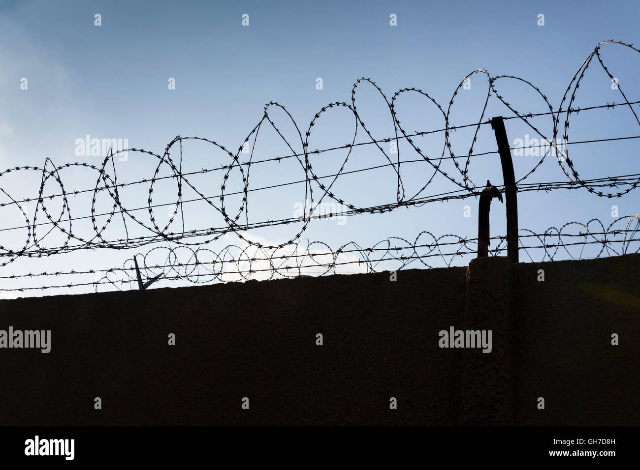 Prison wall barbed wire fence detail with blue sky in background Stock