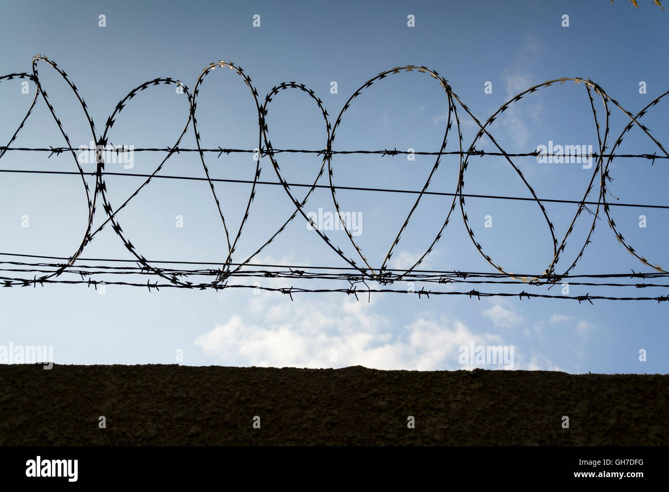 Prison wall barbed wire fence detail with blue sky in background Stock