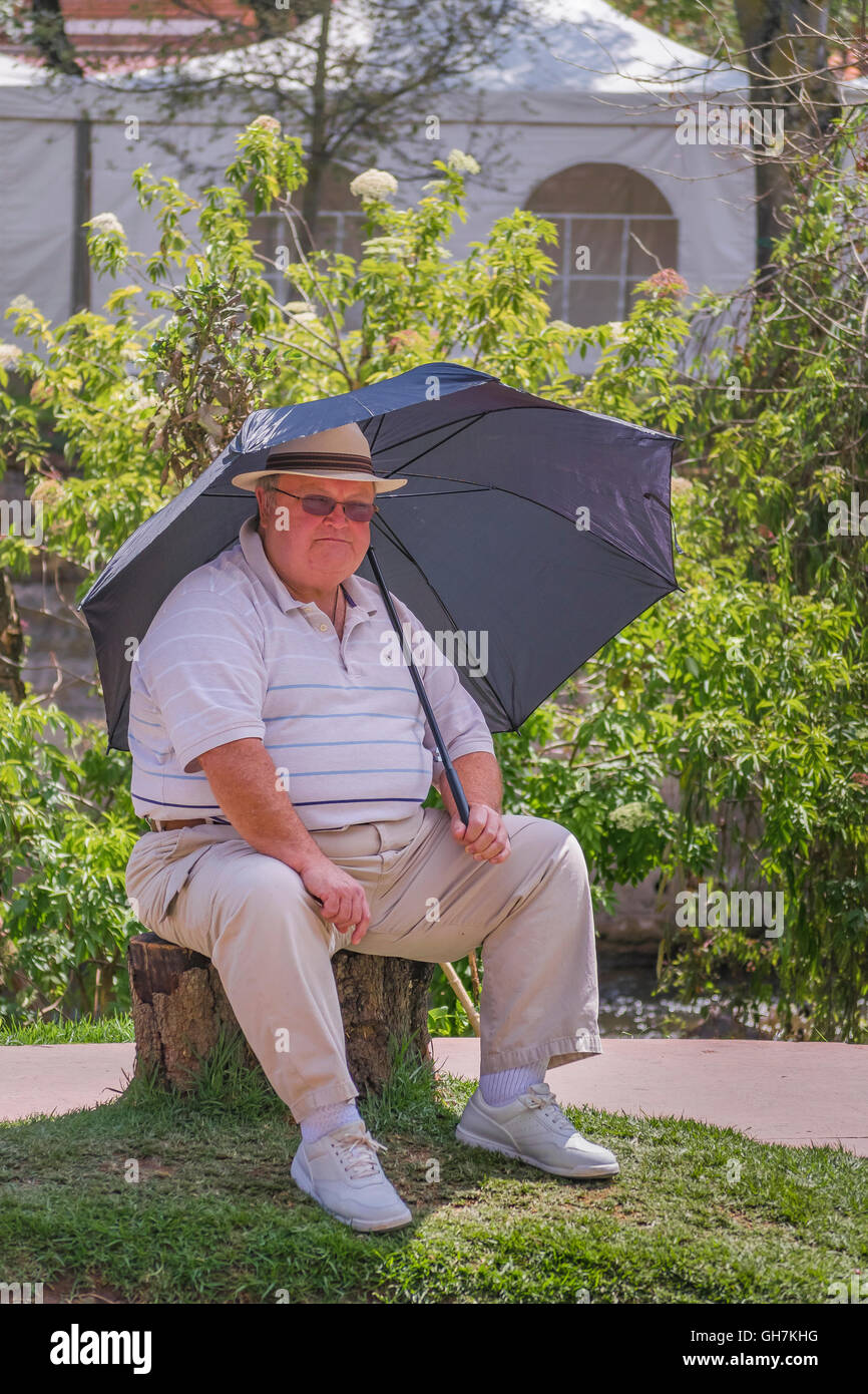 CUENCA, ECUADOR, NOVEMBER - 2015 - Adult fan man with umbrella sitting enjoying the day at park in front of river in Cuenca, Ecu Stock Photo