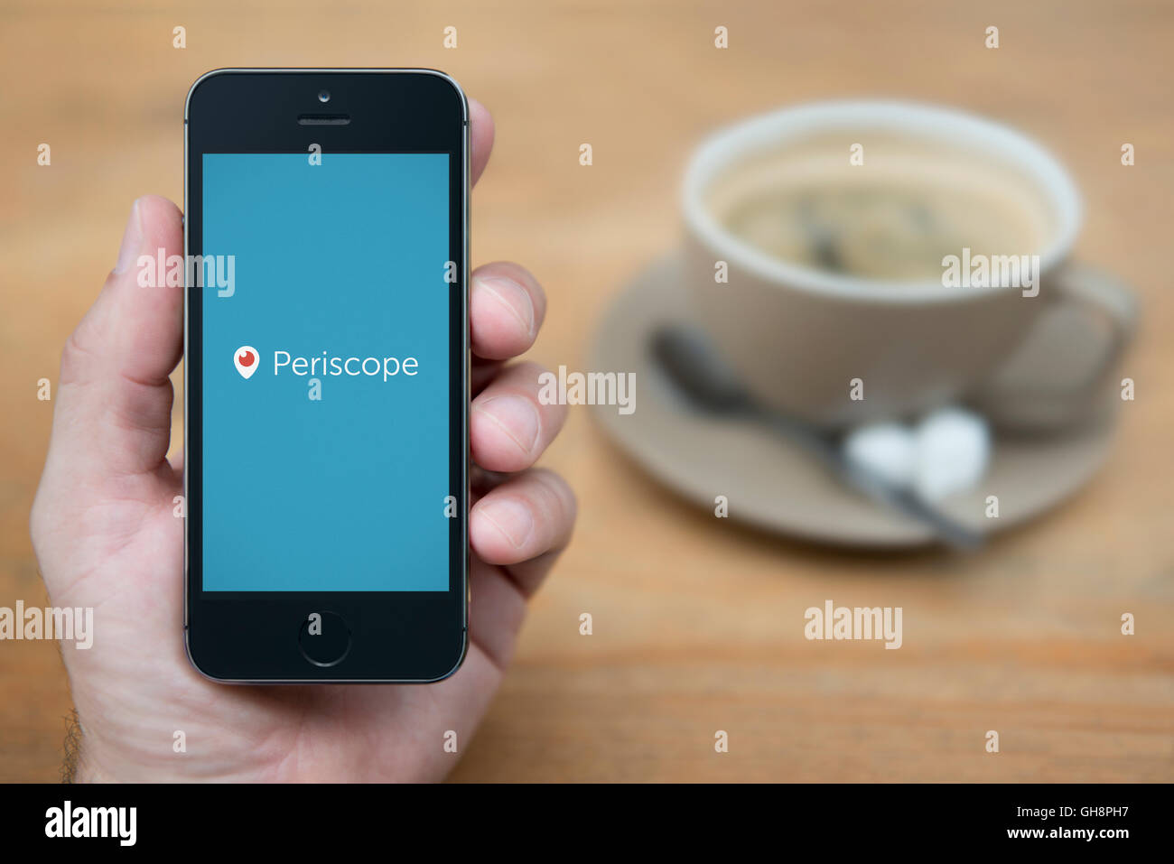 A man looks at his iPhone which displays the Periscope logo, while sat with a cup of coffee (Editorial use only). Stock Photo