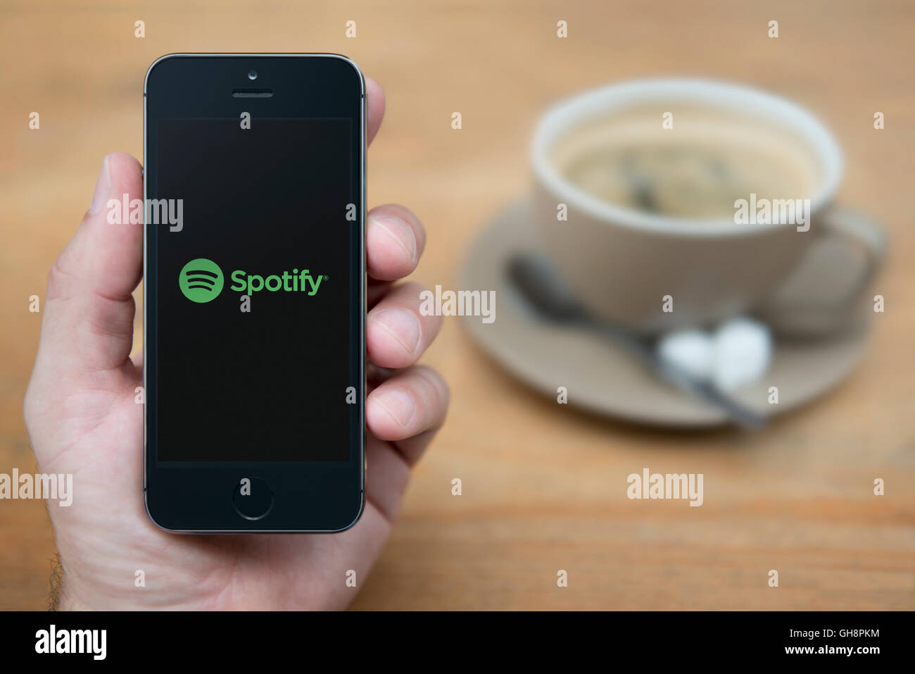 A man looks at his iPhone which displays the Spotify logo, while sat with a cup of coffee (Editorial use only). Stock Photo