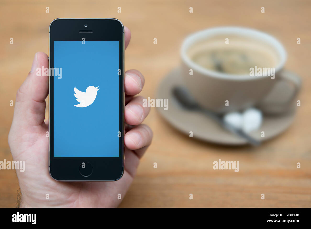 A man looks at his iPhone which displays the Twitter logo, while sat with a cup of coffee (Editorial use only). Stock Photo