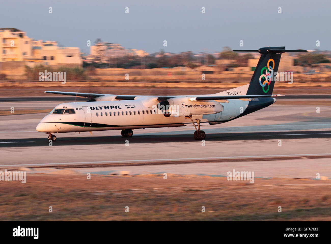Olympic Air Bombardier Dash 8-Q400 propeller airplane taking off at sunset. Slow shutter speed used for panning, prop blur. Turboprop plane takeoff. Stock Photo