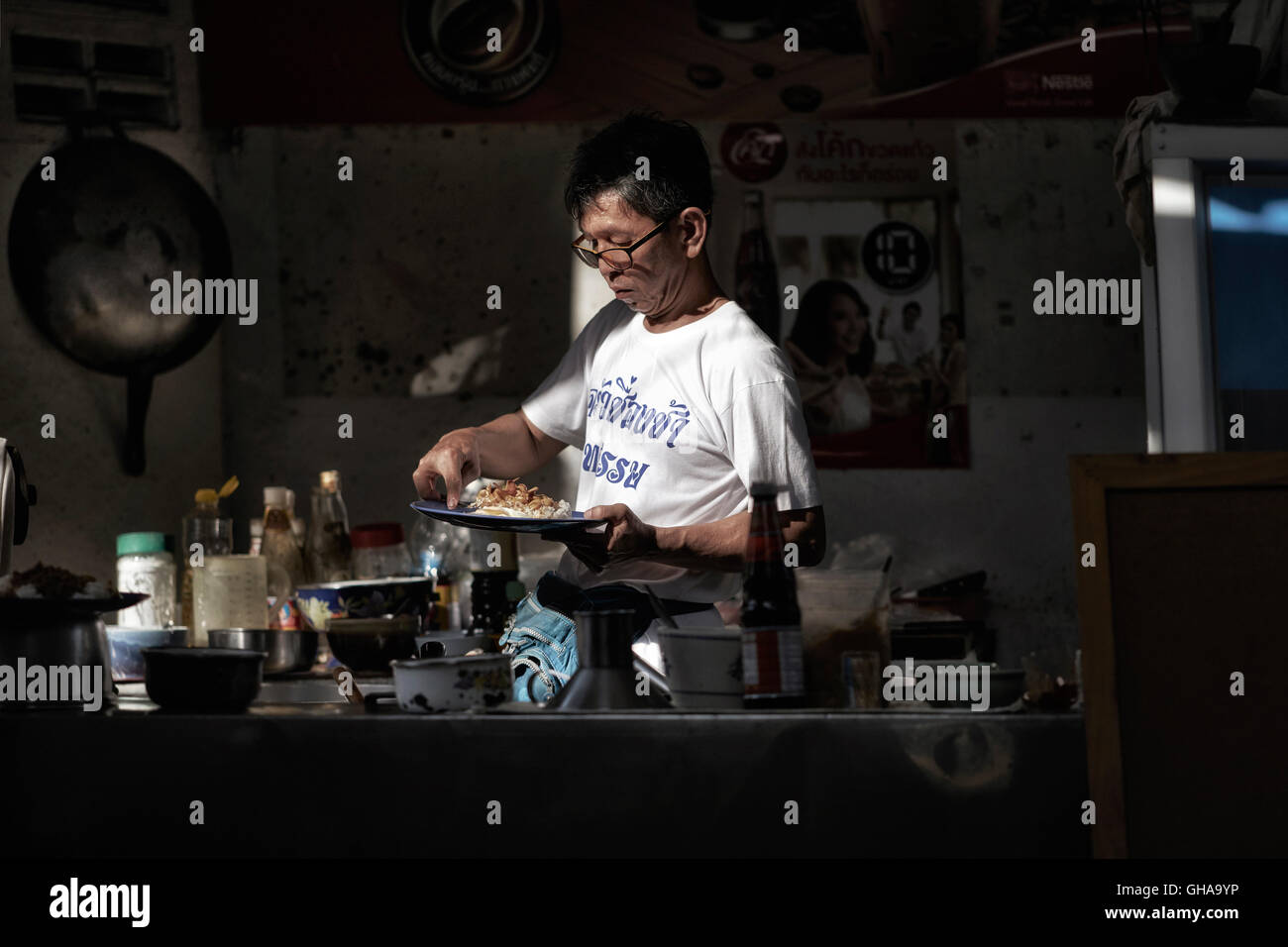 Chef cooking in the shadows at a back street alleyway cafe. Thailand S. E. Asia Stock Photo