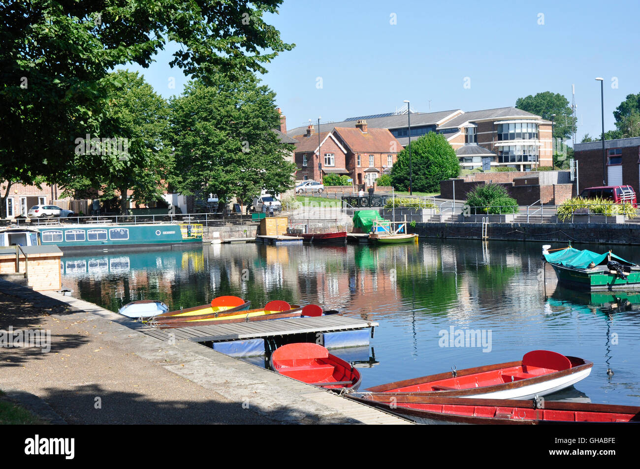 Hampshire - Chichester canal basin - colourful pleasure boats moored - sunlight and shadows - reflections-town skyline backdrop Stock Photo