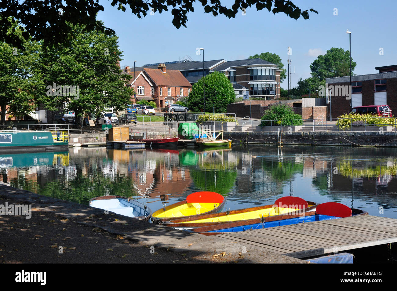 Chichester canal basin - colourful boats moored - summer sunlight and shadows - reflections - town backdrop Stock Photo