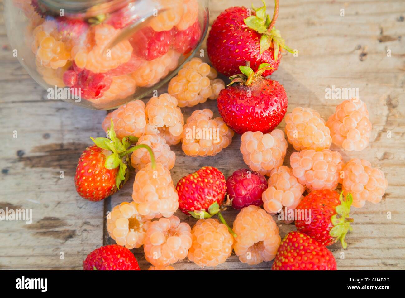 Multicolored raspberries in a glass jar with strawberries on background ...