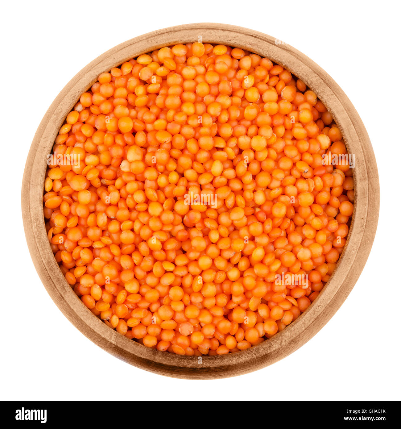 Red lentils in a wooden bowl on white background. Seeds of Lens culinaris, edible raw pulses of the legume family. Stock Photo