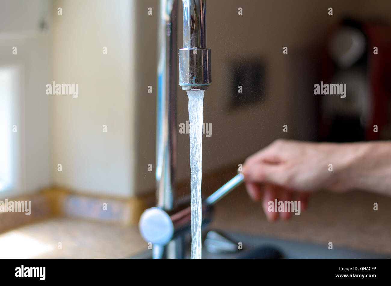 Woman turning on a tap with running water and a chrome faucet indoors in the house, close up of the stream of water Stock Photo
