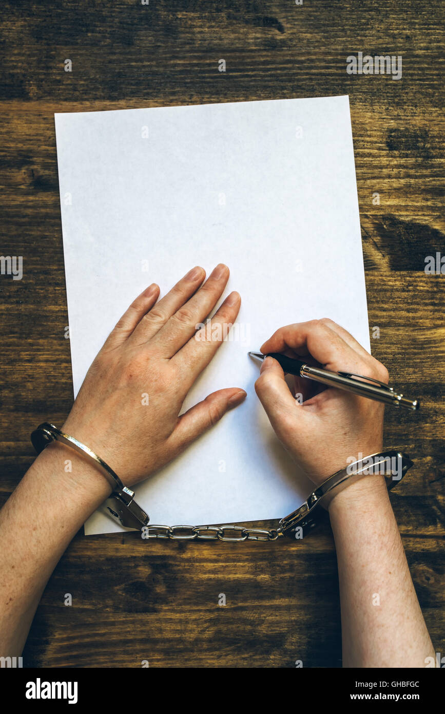 Female hands cuffed signing confession, top view of police investigator detective desk Stock Photo