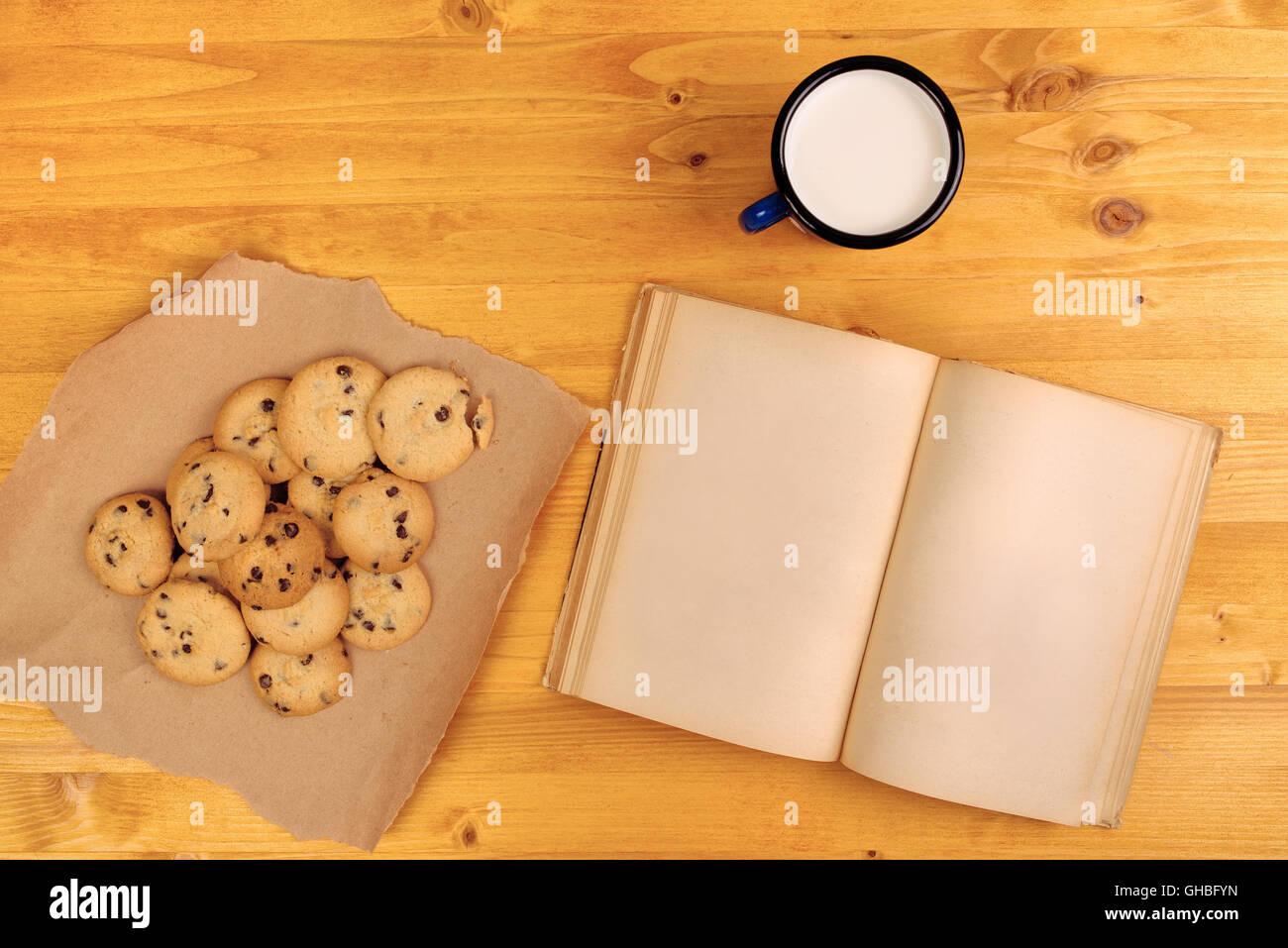 Homemade chocolate chip cookies, milk cup and open book on rustic wooden table, top view Stock Photo