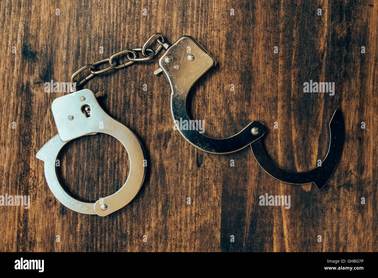 Uncuffed, open hand cuffs on wooden police office desk, top view Stock Photo