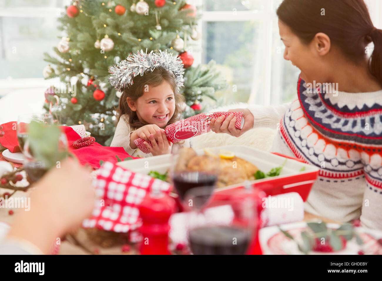 Mother and daughter pulling Christmas cracker at dinner table Stock Photo
