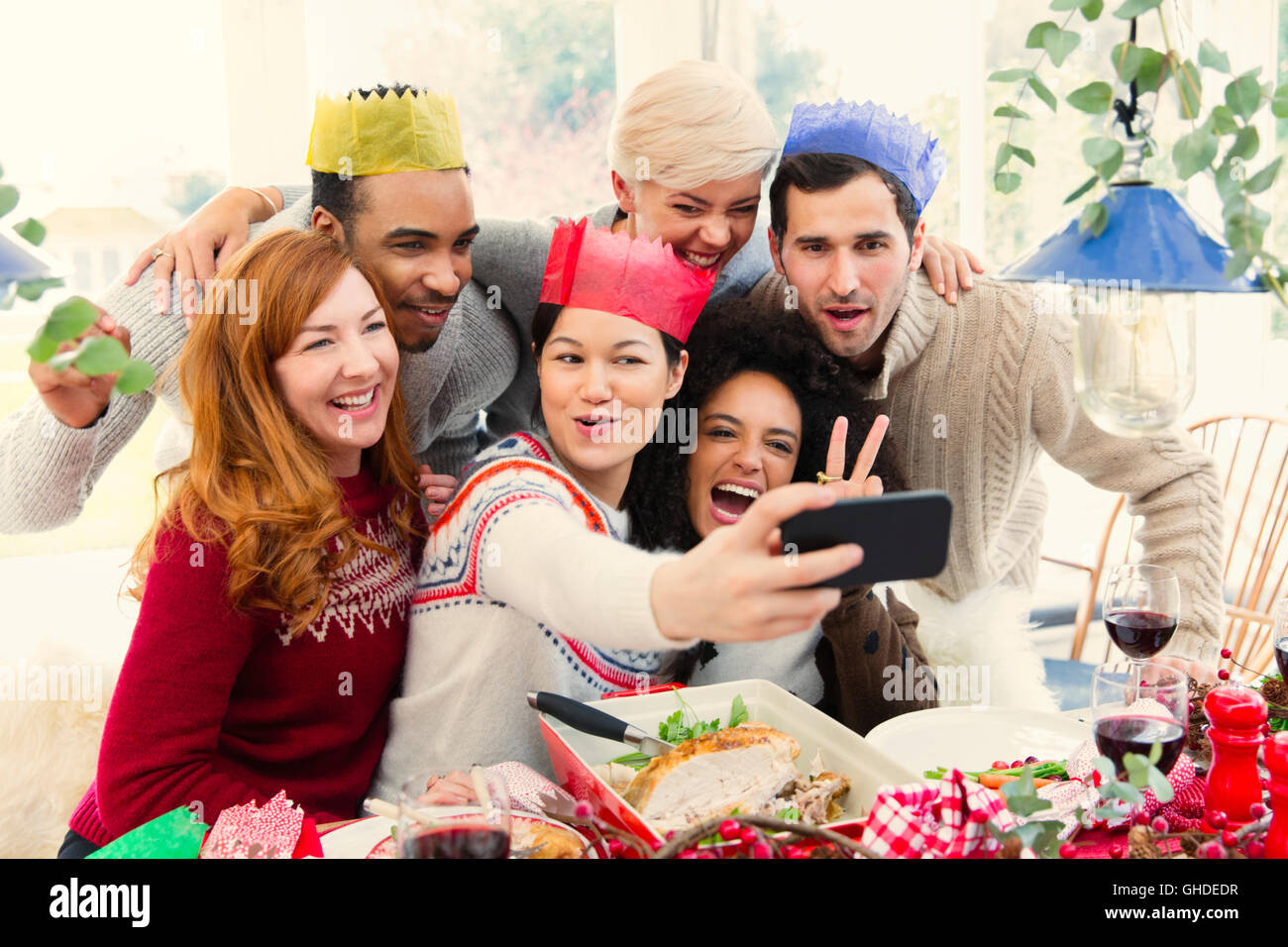 Friends wearing paper crowns taking selfie at Christmas dinner Stock Photo