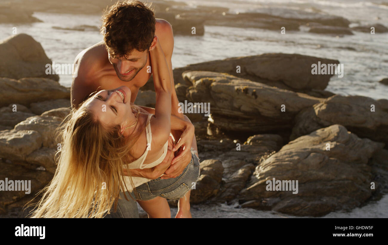 Playful young couple hugging on rocks at ocean Stock Photo