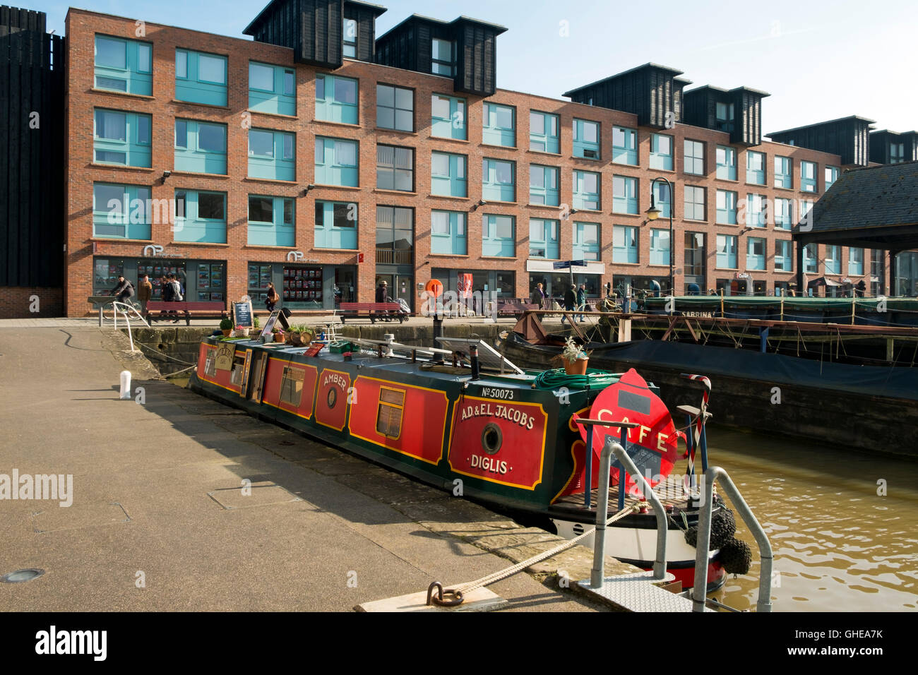 Canal boat cafe moored alongside new build apartments and shops in