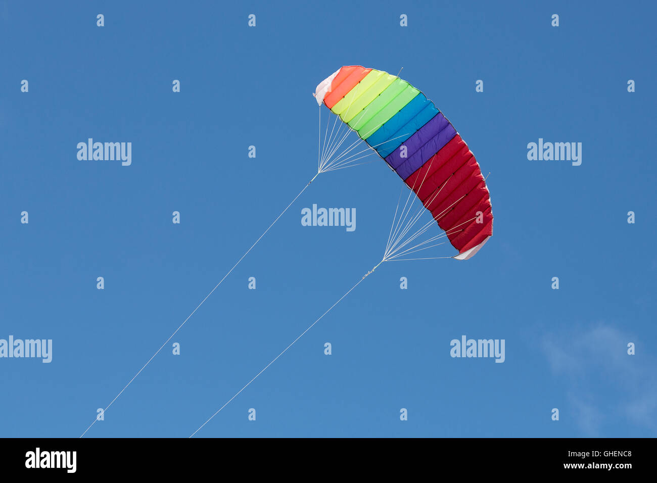 Multi-colored kite flying on a sunny day with a blue sky behind Stock Photo