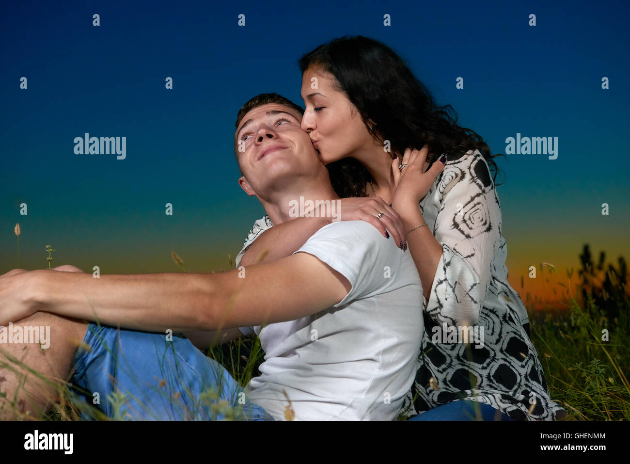 young romantic couple sit on grass and ebmbrace on country outdoor, dark night sky, love concept, adult people Stock Photo