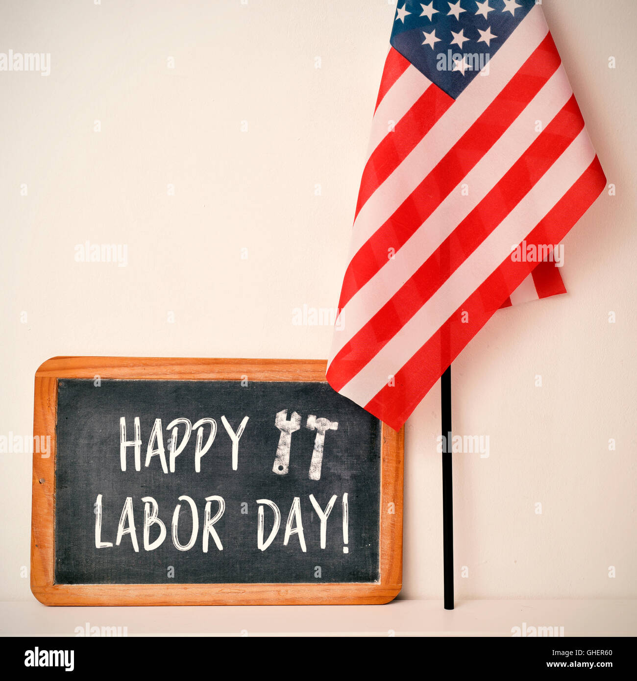 a wooden-framed chalkboard with the text happy labor day written in it and a flag of the United States, against an off-white bac Stock Photo