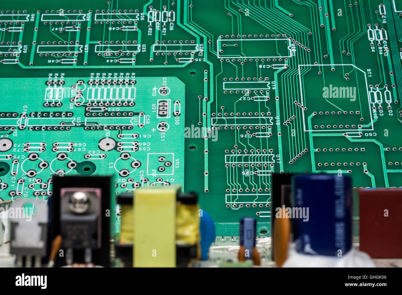 An out-of-focus circuit board with components has a two-tone green printed circuit behind it that is in focus. Stock Photo