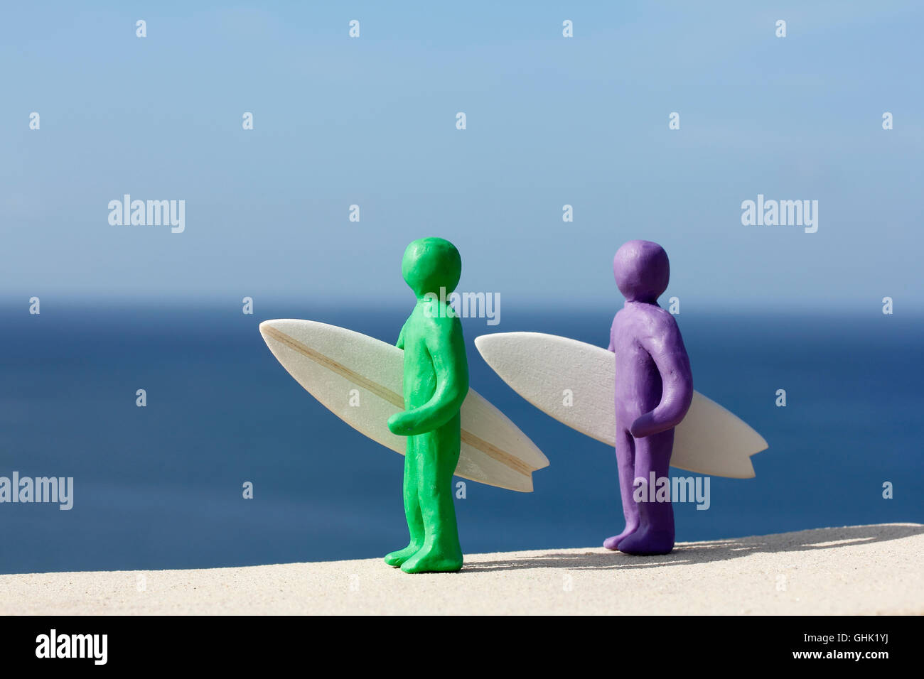 Plasticine people with balsa wood surfboards by the Ocean. Stock Photo
