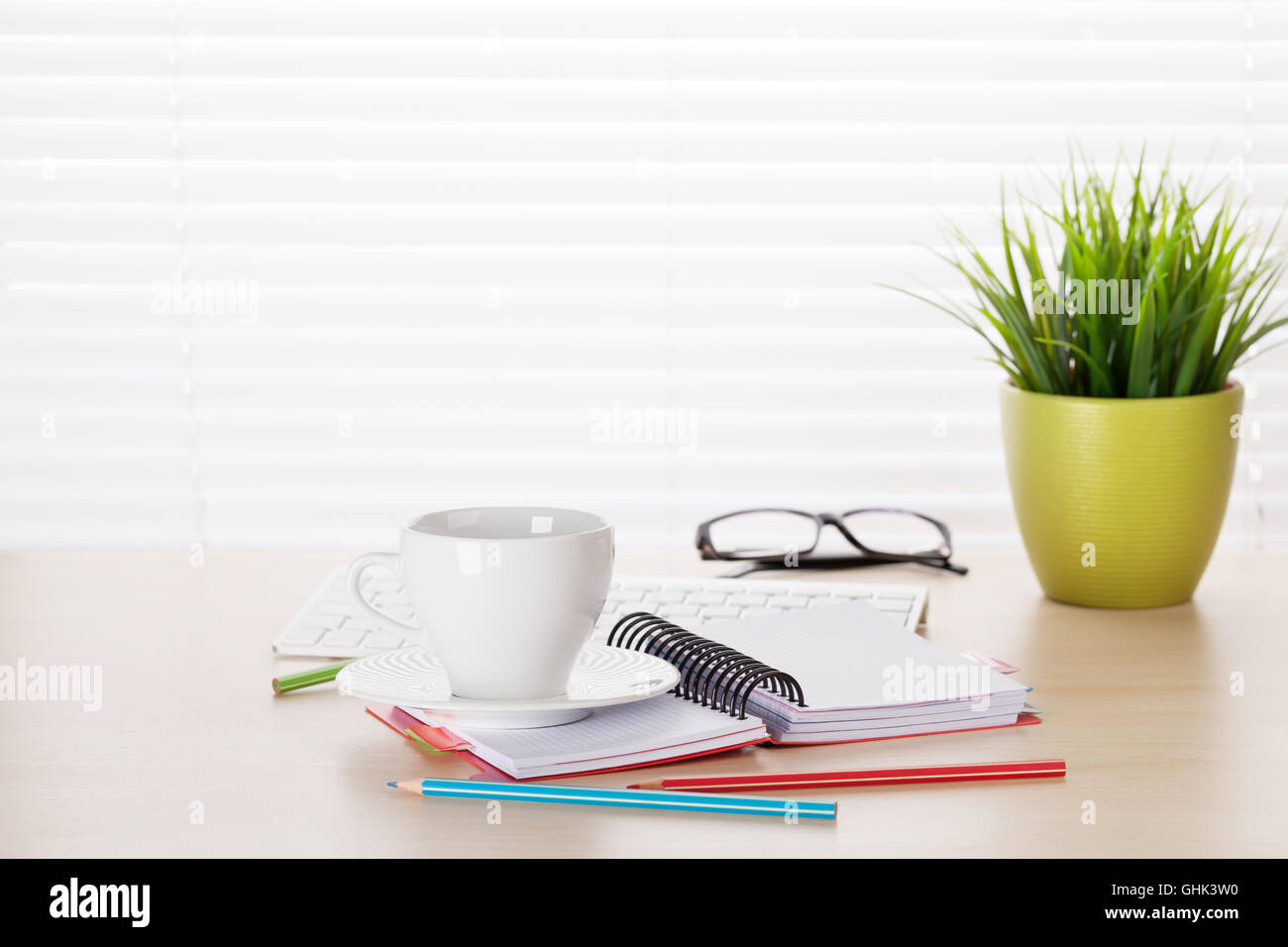 Office workplace with coffee, pc and plant on wooden desk table in front of window with blinds Stock Photo