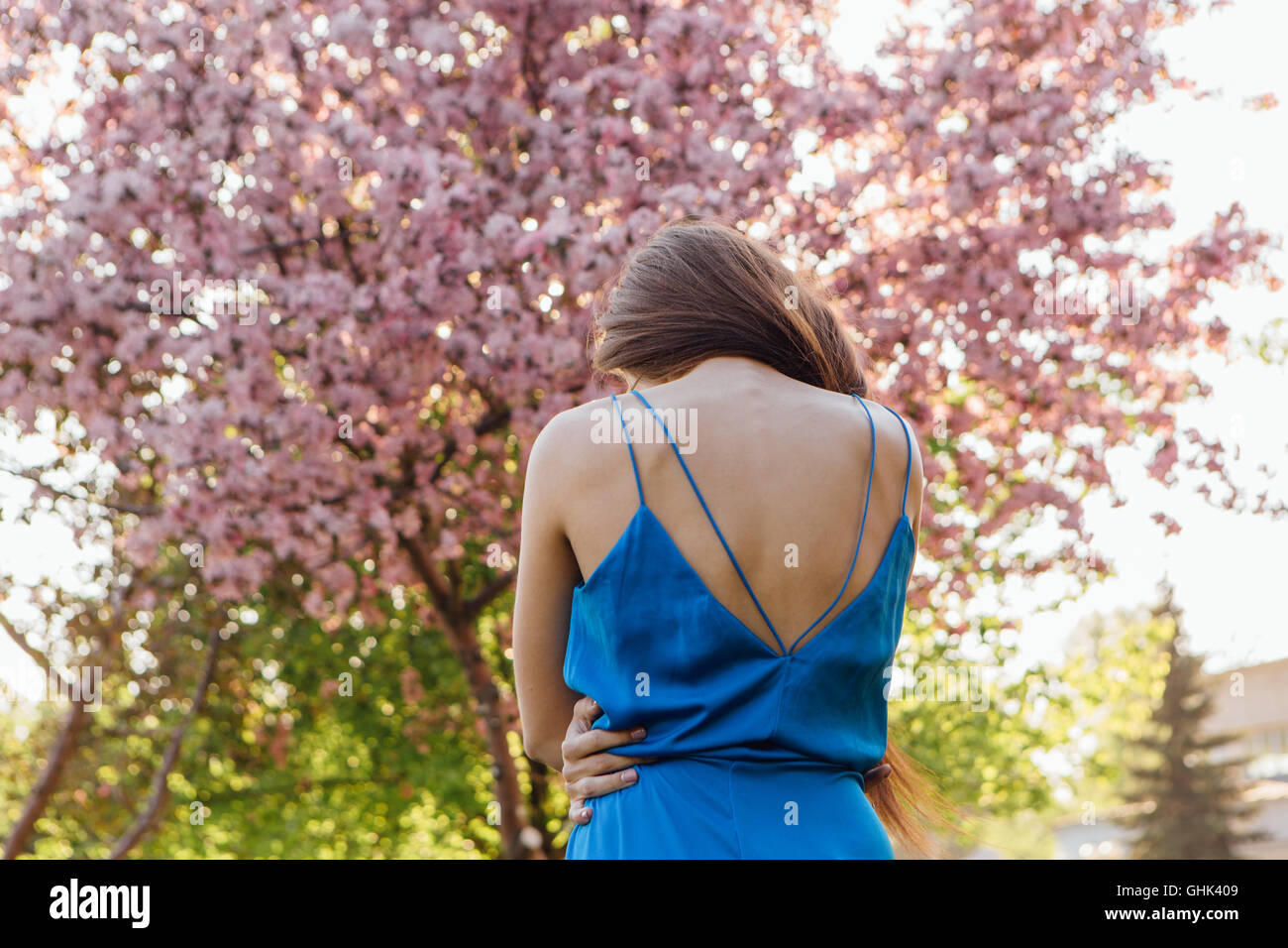 Back view of a beautiful young woman dressed in blue overalls standing ...