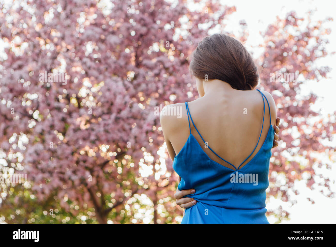 Back view of a beautiful young woman dressed in blue overalls standing ...