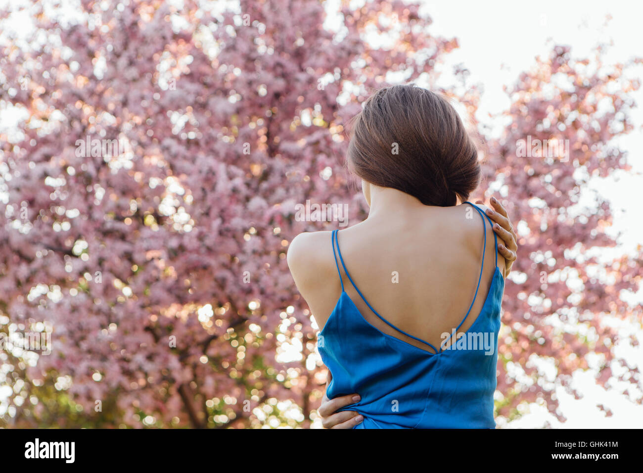 Back view of a beautiful young woman dressed in blue overalls standing ...
