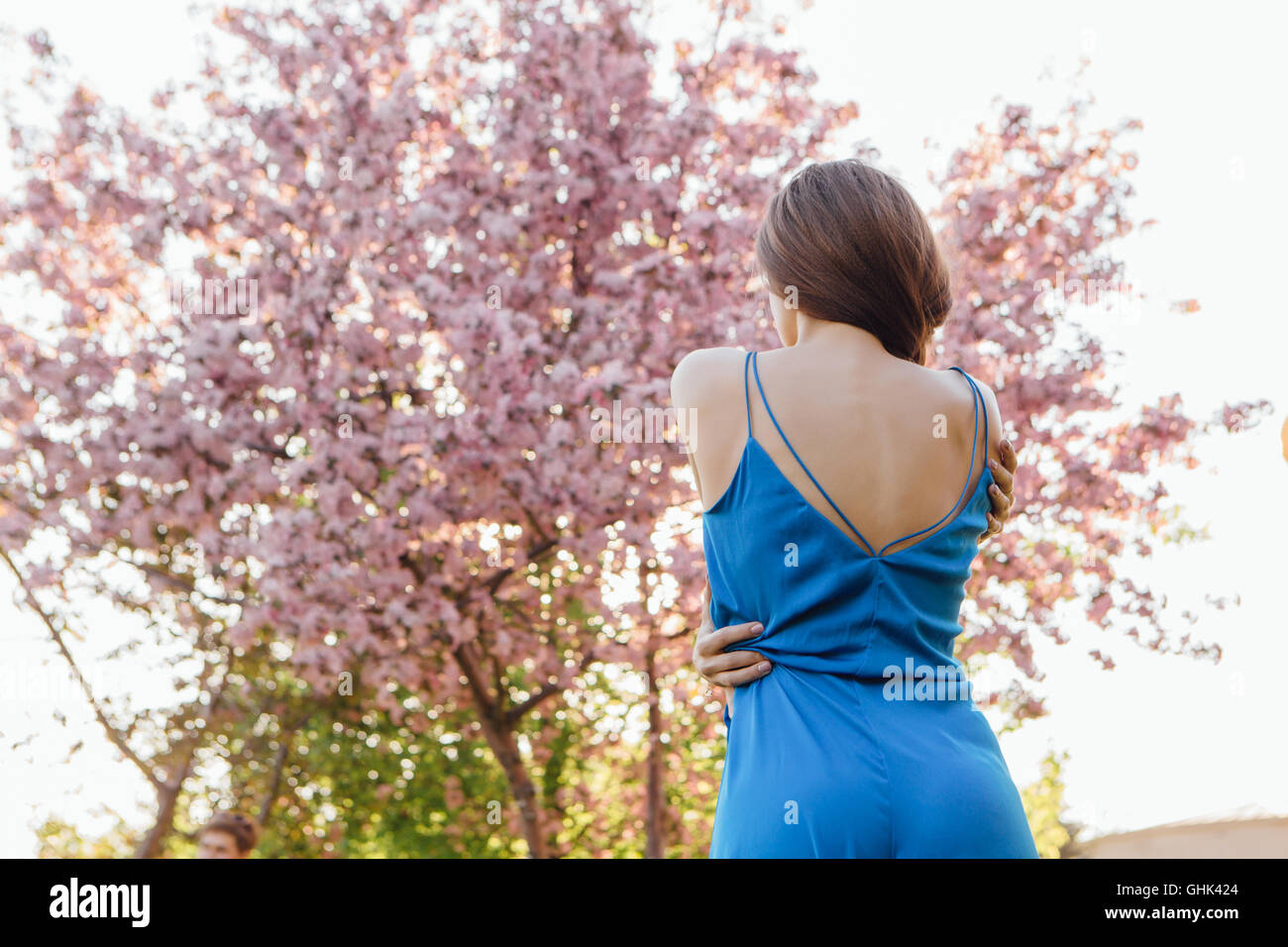 Back view of a beautiful young woman dressed in blue overalls standing ...