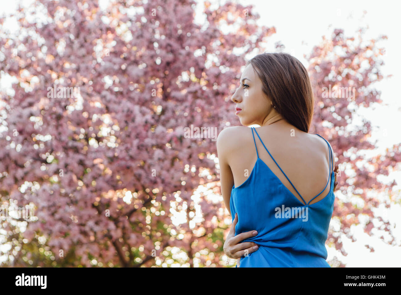 Back view of a beautiful young woman dressed in blue overalls standing ...