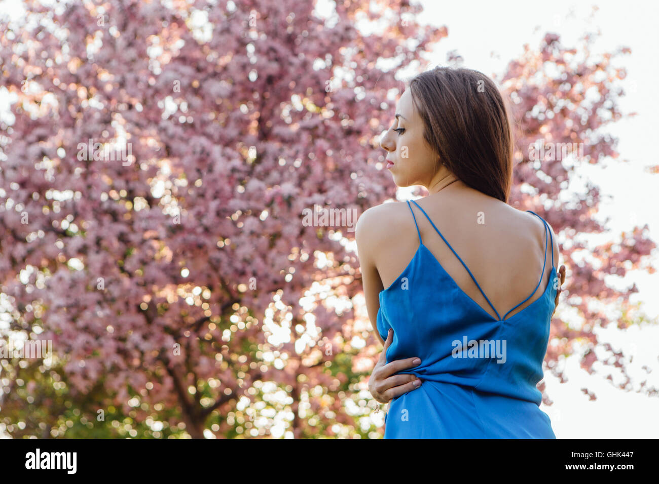 Back view of a beautiful young woman dressed in blue overalls standing ...
